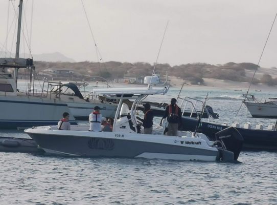 Motorboot in Sao Vicente, Kapverden, bereit zum Angeln im klaren Wasser. Sanddünen und Segelboote im Hintergrund, perfekte Bedingungen für einen Angelurlaub und Abenteuer auf dem Atlantik.