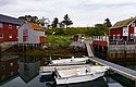 Typisches nordnorwegisches Fischerdorf in Nordland: Rote Holzhäuser am Wasser, Boote an einem Steg, umgeben von grüner Natur. Perfekter Ort für Angelreisen und Erholung in Norwegens beeindruckender Küstenlandschaft.