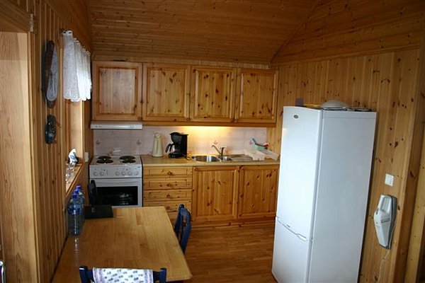 Gemütliche Holzküche in einer Hütte in Nordland, Norwegen, mit Holzschränken, Toaster, Kühlschrank und kleinem Esstisch. Ideal für Angler auf Angelreise, die Komfort und Naturerlebnis kombinieren möchten.