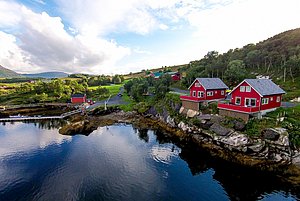 Rote Fischerhütten stehen malerisch an der Küste von Nordland, Norwegen. Klare, spiegelnde Wasserflächen, grüne Hügel und eine idyllische Landschaft laden zum Entdecken und Angeln ein. Perfekt für Angelreisen und Naturerlebnisse.