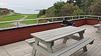 Holzterrasse mit Picknicktisch und Grill, umgeben von grüner Landschaft und Meerblick. Ideal für Angelurlaube in Hitra, Norwegen. Perfekt zum Entspannen nach einem erfolgreichen Angeltag. Outdoor-Genuss pur!