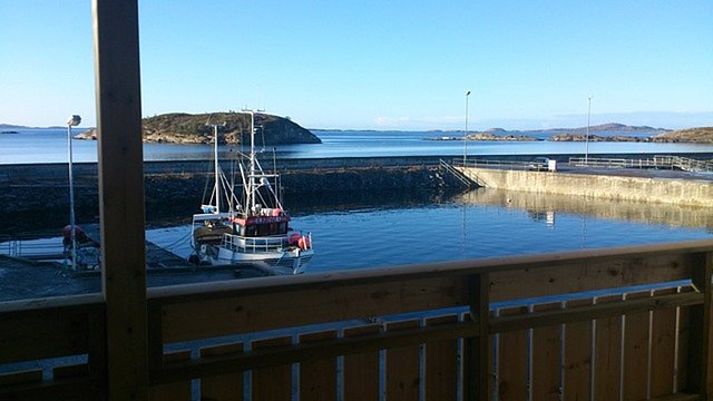 Ein Fischerboot liegt in einem ruhigen Hafen mit Blick auf felsige Inseln im Hintergrund und einem klaren, blauen Himmel.
