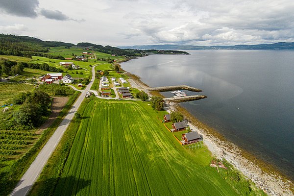 Luftaufnahme einer idyllischen Küstenlandschaft in Hitra, Norwegen. Grüne Felder, traditionelle Häuser und ein kleiner Hafen säumen das ruhige Meer. Perfekte Kulisse für Angelurlaub und Erholung in der Natur.
