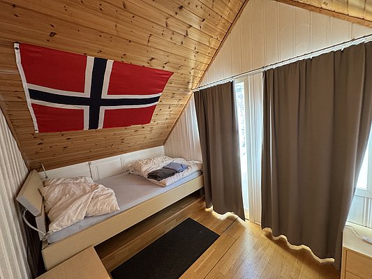 Gemütliches Gästezimmer in Hitra, Norwegen: Holzwände, norwegische Flagge, bequeme Betten, viel Tageslicht. Ideal für Angelliebhaber und Abenteuer in der malerischen Umgebung. Perfekte Unterkunft für entspannte Angelreisen.