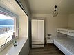 Gemütlicher Raum in Nord-Norwegen mit Etagenbett, Schrank, Nachttisch und Lampe. Großes Fenster mit Blick auf das Meer und Berge. Ideal für Angelurlaub in naturnaher, entspannter Umgebung.