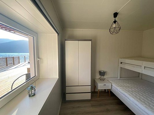 Gemütlicher Raum in Nord-Norwegen mit Etagenbett, Schrank, Nachttisch und Lampe. Großes Fenster mit Blick auf das Meer und Berge. Ideal für Angelurlaub in naturnaher, entspannter Umgebung.