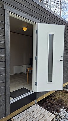 Modernes Holzhaus mit weißem Fenster, umgeben von Natur. Innenansicht zeigt helle Wände, minimalistisches Interieur. Ideal für Angelurlaub in Nordland, Norwegen, um Natur und Ruhe zu genießen. Perfekt für Abenteuer und Entspannung.