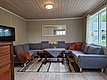 Gemütliches Wohnzimmer in Nordland, Norwegen, mit grauem Ecksofa, Holztisch, Teppich und Fensterblick ins Grüne. Perfekt für entspannte Abende nach einem erfolgreichen Angelausflug. Ideal für Angelreisen und Naturerlebnisse.