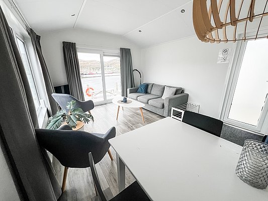 Gemütliches Wohnzimmer in Nord-Norwegen mit moderner Einrichtung. Große Fenster bieten Ausblick auf den Hafen. Ideal für Angelurlauber, die Komfort und skandinavische Landschaft genießen möchten. Perfekter Rückzugsort nach einem erfolgreichen Angeltag.