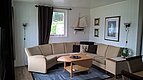 Gemütliches Wohnzimmer in Nord-Norwegen mit heller Eckcouch, stilvollen Wanddekorationen und maritimen Akzenten. Ideal für Entspannung nach dem Angelurlaub, bietet weiche Beleuchtung und einen einladenden Ausblick auf grüne Landschaft.