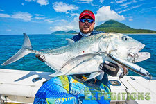 Ein Angler hält einen beeindruckenden Fisch im strahlend blauen Meer vor der Küste Tansanias. Im Hintergrund sind grüne Inseln und ein klarer Himmel zu sehen. Perfekte Bedingungen für einen erfolgreichen Angelurlaub.