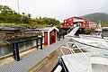 Rote Fischerhütten und Boote an einem ruhigen Steg im idyllischen Nordland, Norwegen. Perfekter Ausgangspunkt für Angelfreunde. Malerische Landschaft im typisch skandinavischen Stil, umgeben von grünen Hügeln und ruhigem Wasser.