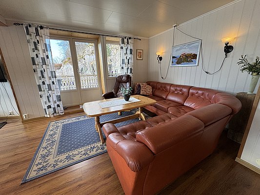 Gemütliches Wohnzimmer in Hitra, Norwegen: Große Ledercouch, Holztisch und stilvolle Wandbeleuchtung vor Panoramafenstern mit Blick auf Felsen. Ideal für entspannte Angelurlaube mit wohnlicher Atmosphäre. #Angelurlaub #Hitra #Norwegen