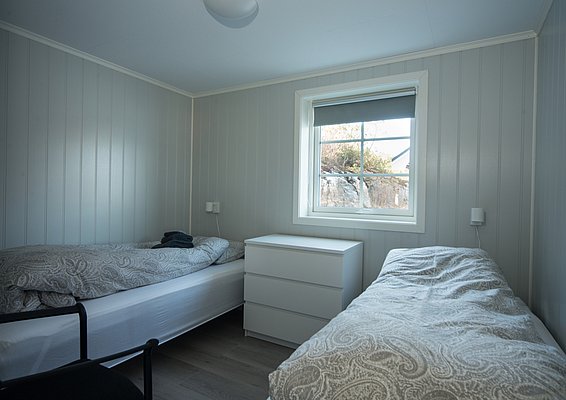 Helles Schlafzimmer mit zwei Einzelbetten, einem zentralen weißen Nachttisch und einem Fenster mit Blick nach draußen.