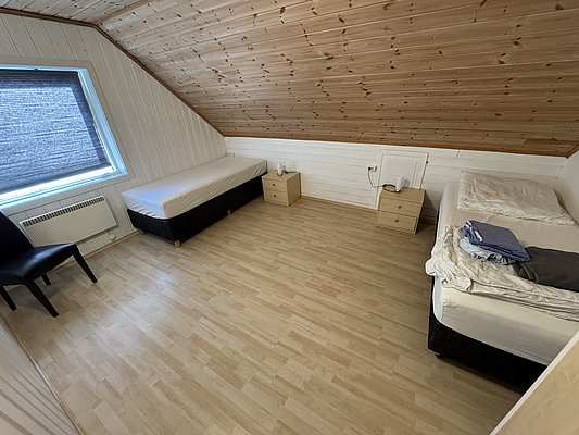 Gemütliches Zimmer in Hitra, Norwegen, mit zwei Betten, Holzdecke und großem Fenster. Perfekt für Angler, die Ruhe und Komfort suchen. Ideal gelegen für den nächsten Angelurlaub.