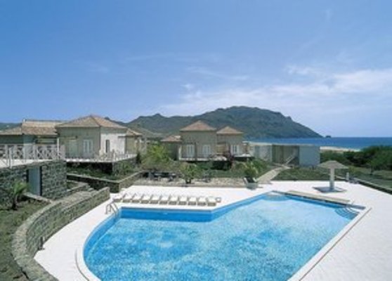 Ein luxuriöser Außenpool mit Liegestühlen vor einer Reihe von eleganten Steincottages, umgeben von einer beeindruckenden Berglandschaft und blauem Himmel. Ein luxuriöser Außenpool mit Liegestühlen vor einer Reihe von eleganten Steincottages, umgeben von einer beeindruckenden Berglandschaft und blauem Himmel.