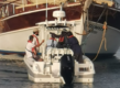 Kleines Boot im Hafen von São Vicente, Kapverden, nahe großem Holzschiff. Personen an Bord bereiten sich auf eine Angeltour vor. Perfekte Kulisse für einen abenteuerlichen Angelurlaub.