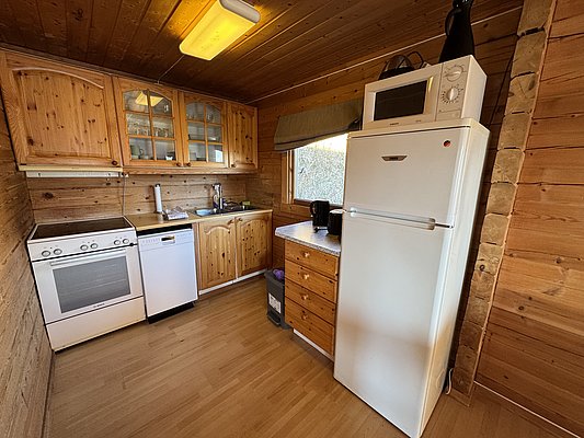 Gemütliche Holzküche in einer norwegischen Ferienhütte auf Hitra. Ausgestattet mit Herd, Kühlschrank, Geschirrspüler und Mikrowelle. Perfekt für Angelreisende, die Komfort und Funktionalität suchen. Ideal für Selbstversorger im Angelurlaub in Norwegen.