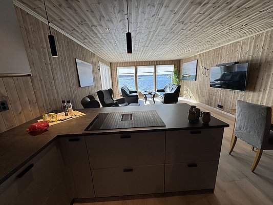 Gemütliches Ferienhaus auf Hitra, Norwegen. Holzverkleidung, moderne Küche, geräumiger Wohnbereich mit Blick aufs Meer. Perfekt für Angelurlaub und Entspannung am Fjord. Große Fensterflut lassen viel Licht herein. Ideal für Abenteuer und Erholung.