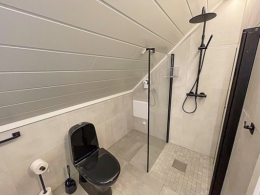 Modernes Badezimmer in Nord-Norwegen mit schwarzer Toilette, geräumiger Dusche und stilvollem Design. Perfekt für Entspannung nach einem erfolgreichen Angeltag. Skandinavische Eleganz trifft auf Funktionalität in einem gemütlichen Rückzugsort. Ideal für Angelurlaubsunterkünfte.