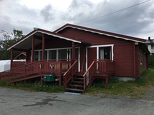 Rotes Holzhaus in Nord-Norwegen vor bewölktem Himmel. Traditionelles skandinavisches Design, umgeben von grüner Wiese. Perfekt für Angelurlaub und entspannende Aufenthalte im Einklang mit der Natur. Ideal für Entdecker und Erholungssuchende.