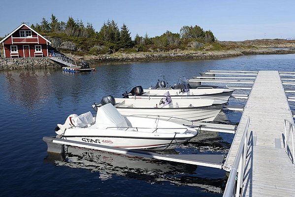 Das Bild zeigt Boote am Steg vor einem roten Ferienhaus auf Hitra, Norwegen. Ideal für Angelurlaub, umgeben von malerischer Natur und klaren Gewässern. Perfekt zum Meeresangeln und Entspannen in skandinavischer Idylle.