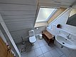 Helles Badezimmer in Hitra, Norwegen: Schrägdachfenster, weiße Fliesen, Waschbecken, Toilette, rollbarer Holzregal, grüner Pflanzendekor, Toilettenpapierhalter. Ideal für komfortablen Angelurlaub.