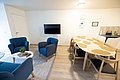 Gemütliches Wohnzimmer in Nordland, Norwegen: Blaue Sessel, moderner Fernseher, großer Esstisch und Küchenzeile. Ideal für Angelurlaub mit entspanntem Ambiente. Perfekter Ort zum Erholen nach einem erfolgreichen Tag am Wasser.