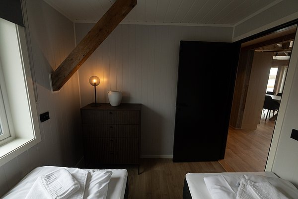 Gemütliches Schlafzimmer in Nordland, Norwegen: Zwei Betten, warme Beleuchtung, rustikaler Holzbalken, modernes Interieur. Ideal für erholsamen Angelurlaub. Entspannung und Komfort in malerischer Umgebung.