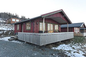 Rote Holzhütte mit Veranda in Hitra, Norwegen, umgeben von schneebedecktem Boden und Wäldern. Perfekter Ausgangspunkt für Angelreisen und Naturerlebnisse in malerischer Umgebung. Entspannung und Abenteuer vereint.