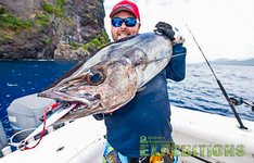 Ein Angler hält einen großen Fisch auf einem Boot vor einer felsigen Küste in Tansania. Im Vordergrund ist ein beeindruckender Fang, ideal für ein Angelabenteuer in Afrika. Klarer Himmel und tiefblaues Wasser.