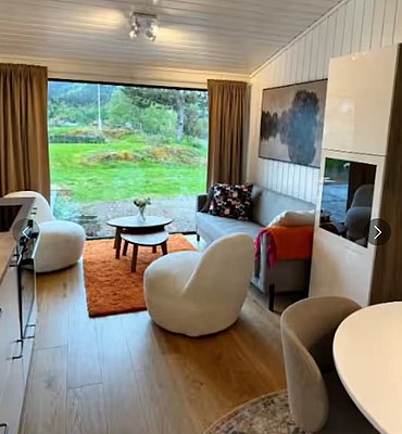 Gemütliches Wohnzimmer auf Hitra mit Panoramablick ins Grüne. Moderne Einrichtung mit bequemen Sesseln, Sofa und dekorativem Teppich. Perfekt zum Entspannen nach einem erlebnisreichen Angelurlaub in Norwegen.