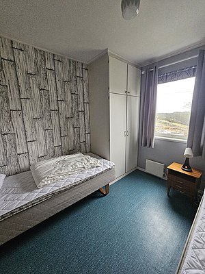 Gemütliches Zimmer mit Einzelbett, Schrank und Fensterblick auf malerische norwegische Landschaft in Südwest-Norwegen. Perfekter Rückzugsort nach einem erfolgreichen Angeltag. Ideal für Angelreisende, die Ruhe und Komfort suchen.