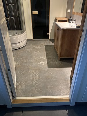 Gemütliches Badezimmer in Nord-Norwegen mit moderner Dusche, Holzwaschtisch und verziertem Steinboden. Ideal nach einem erlebnisreichen Angeltag zum Entspannen und Frischmachen. Perfektes Zusammenspiel von Komfort und skandinavischem Stil.