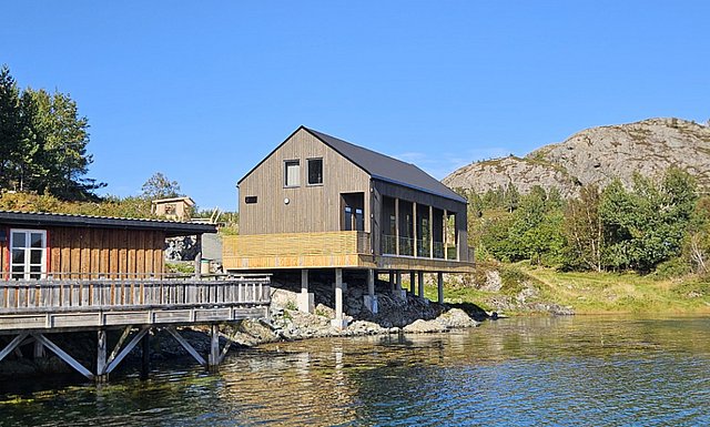 Küstenhütte in Hitra, Norwegen: modernes Holzhaus mit Terrasse am Wasser, umgeben von Felsen und grüner Natur. Ideal für Angelreisen und Entspannung in malerischer Landschaft. Perfekte Unterkunft für Abenteuer und Erholung.
