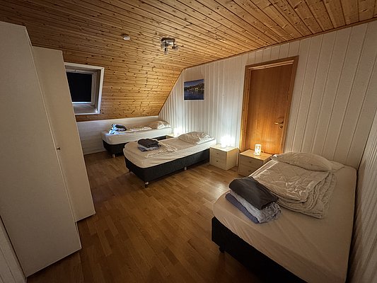 Ein gemütliches Schlafzimmer mit drei Einzelbetten, Holzboden und Vertäfelung. Nachtlichter sorgen für sanfte Beleuchtung. Perfekt für erholsame Nächte nach einem erfolgreichen Angelabenteuer in der Region Hitra, Norwegen.