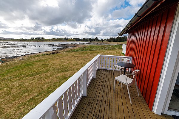 Idyllische Küstenlandschaft bei Hitra, Norwegen: Rotes Ferienhaus mit Terrasse, Meerblick und grasbewachsene Ufer. Perfekt für Angelreisende auf der Suche nach Entspannung und Naturerlebnissen. Optimaler Startpunkt für unvergessliche Angelabenteuer im hohen Norden.