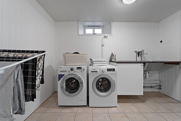 Heller Hauswirtschaftsraum in Nord-Norwegen mit Waschmaschine, Trockner und Waschbecken. Handtücher und Waschmittel ergänzen die funktionale Einrichtung. Perfekt für längere Angelaufenthalte.
