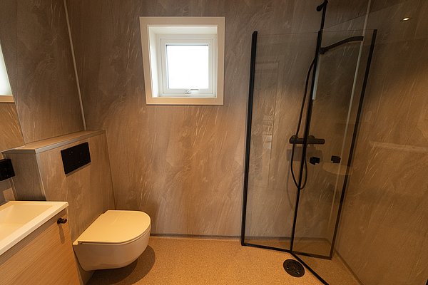 Modernes Badezimmer in Nordland, Norwegen, mit eleganter Dusche, hochmodernem WC und stilvollen Holzwänden. Ideal für Angelreisen mit Komfort. Helles Fenster sorgt für natürliches Licht. Perfekte Kombination aus Funktionalität und skandinavischem Design.