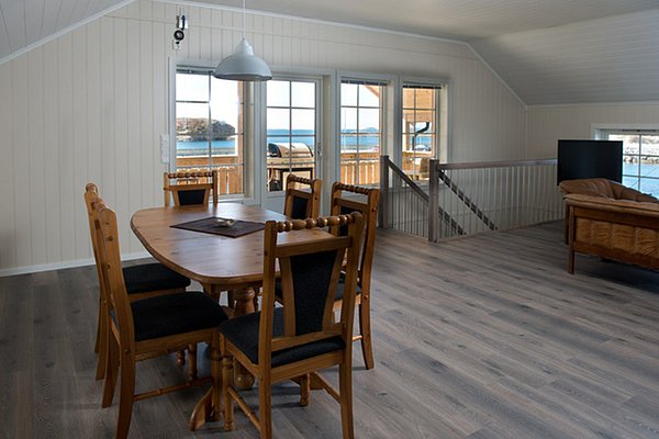 Helles und modernes Wohnzimmer mit Holzmöbeln, Blick durch große Fenster auf das Meer und eine Terrasse.