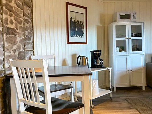 Gemütliche Küchenecke in Nord-Norwegen mit Holzmöbeln, Kaffeemaschine und Wasserkocher. Ideale Basis für Angelreisen, um nach einem erfolgreichen Fang zu entspannen. Rustikales Ambiente mit Steinwand einladend und warm gestaltet.