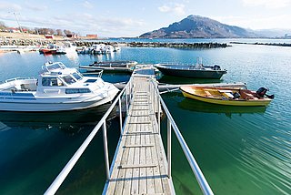 Ein malerischer Steg mit Booten in der Region Nordland, Norwegen. Klare Gewässer, Berge im Hintergrund und strahlender Himmel – ideal für Angelreisen und maritime Abenteuer. Perfektes Ziel für Naturliebhaber und Angler.