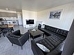 Das Bild zeigt ein modernes Wohnzimmer in Norwegen mit schwarzem Ledersofa, Flachbildfernseher und Küchenbereich. Perfekt für Angelreisende in Hitra, die Komfort und Gemütlichkeit nach einem erfolgreichen Fischen genießen möchten.