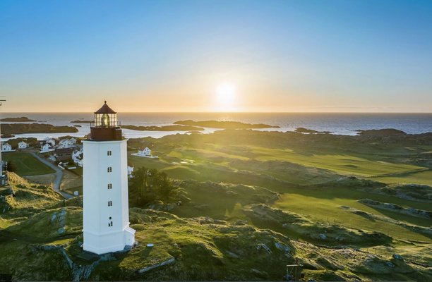 Ein Leuchtturm steht auf einer grünen Küstenlandschaft, während die Sonne über dem ruhigen Meer und kleinen Inseln am Horizont untergeht. Ein Leuchtturm steht auf einer grünen Küstenlandschaft, während die Sonne über dem ruhigen Meer und kleinen Inseln am Horizont untergeht.