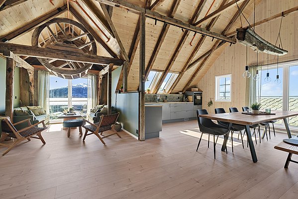 Gemütlicher Wohnbereich in Südwest-Norwegen; modernes, rustikales Interieur mit Holzbalken, heller Einrichtung und großen Fenstern mit Blick auf schneebedeckte Berge. Perfekt für einen entspannten Angelurlaub und Naturgenuss.