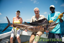 Drei Angler auf den Malediven halten einen großen, beeindruckenden Fisch an Bord eines Bootes. Strahlend blauer Himmel und Meer im Hintergrund, ideal für begeisterte Angelreisen und Abenteuer auf hoher See.
