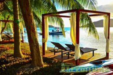 Sonnige Küstenszene in Südwest-Norwegen: Palmen, gemütliche Liegestühle unter Pavillons am Wasser. Im Hintergrund ein Boot auf glasklarem Meer. Perfekte Kulisse für entspannten Angelurlaub und Abenteuer in idyllischer Umgebung.