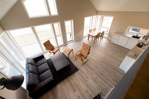 Moderne skandinavische Ferienwohnung in Nordland, Norwegen. Helles Wohnzimmer mit großen Fenstern, gemütlicher Sitzecke und Essbereich. Ideal für erholsame Angelurlaube mit atemberaubendem Blick. Komfort trifft auf stilvolle Einfachheit.