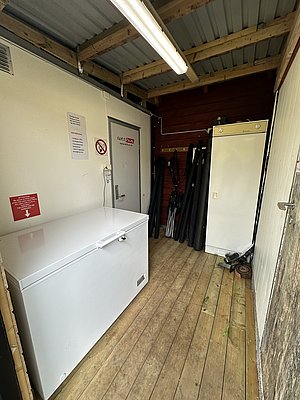 Gefrierschrankraum in Nord-Norwegen mit Holzboden und Angelzubehör. Die robuste Einrichtung bietet Anglern ideale Bedingungen zur Lagerung von Fang und Ausrüstung. Perfekt für deinen Angelurlaub in malerischer Umgebung. Petri Heil!