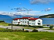 Weißes Gebäude mit rotem Dach in Sudavik, Island. Malerische Landschaft mit Bergen und Meer im Hintergrund, grüner Rasen im Vordergrund. Perfekter Ort für Erholung und Naturliebhaber. Ideal für Angelreisen und Entdeckungstouren.